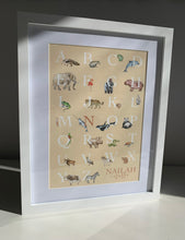 Load image into Gallery viewer, Personalised Kids' Animal Alphabet Poster in a neutral, sand colour. Featuring watercolour animals corresponding to the alphabet. Personalised with a child's full name. Framed and placed on a shelf in a child's room.
